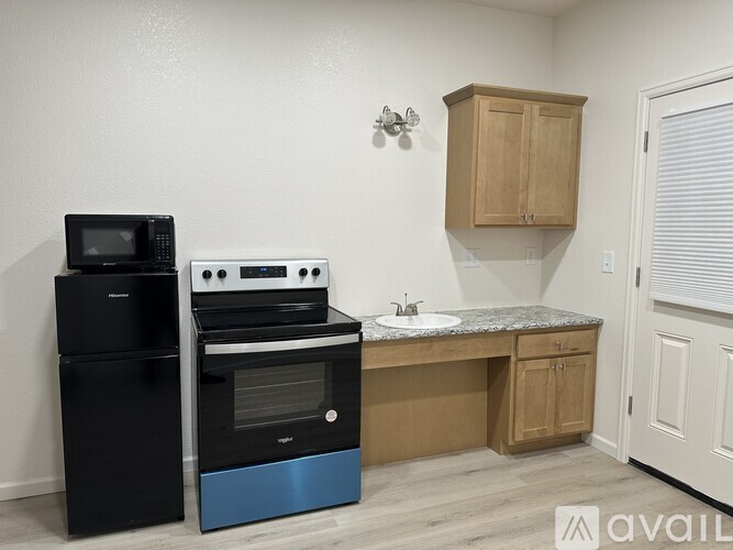 A kitchen with a black fridge, a black oven, a black microwave, a granite countertop, wooden cabinets, and a white door.