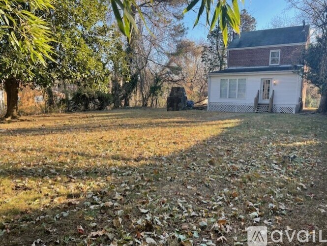 A house with a white fence is surrounded by trees and a grassy area with fallen leaves.