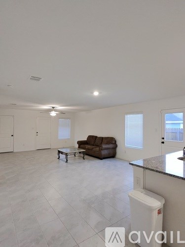 A spacious living room with a brown leather couch and a white trash bin.