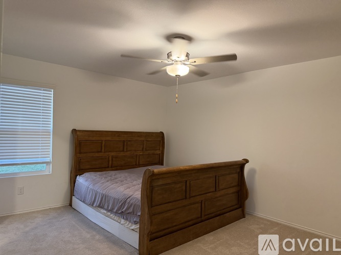 A bedroom with a bed, ceiling fan, and window with blinds.