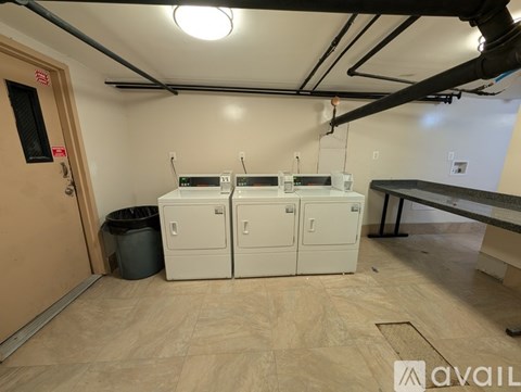 A room with a brown door, a trash can, and a row of white cabinets.