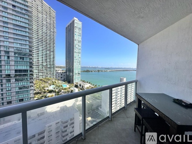 A balcony with a table and chairs overlooks a cityscape with a body of water.