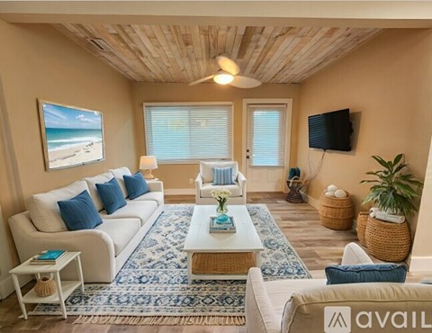 A living room with a white sofa, a blue rug, and a wooden ceiling.