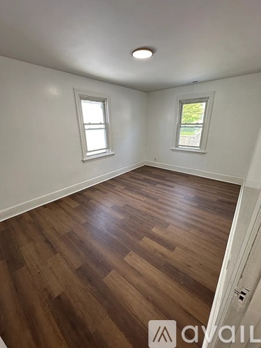 A room with wooden flooring and two windows.