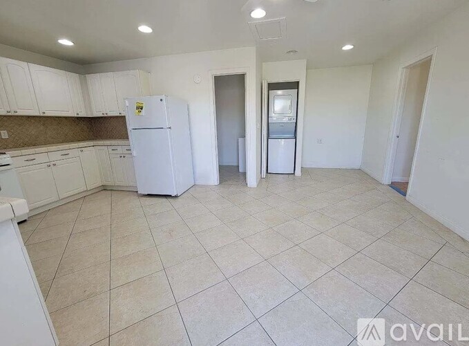 A white refrigerator is in a room with tiled flooring and white walls.