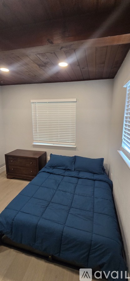 A bedroom with a bed, nightstand, and window with blinds.