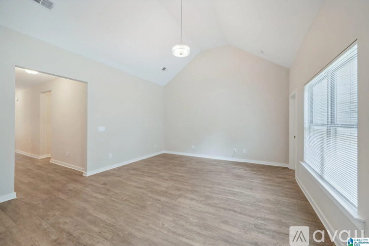 A spacious room with wooden flooring and a window with blinds.