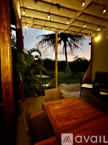 A wooden table and chairs are set up on a patio with a view of the sky and trees.