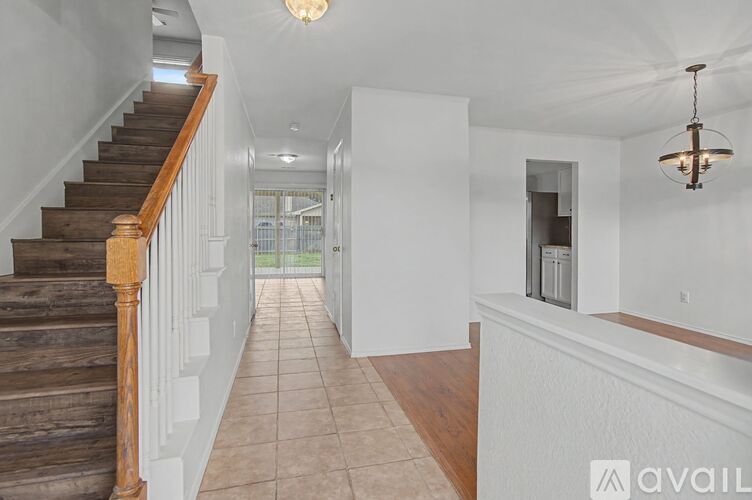 A hallway with a staircase on the left and a chandelier hanging from the ceiling.
