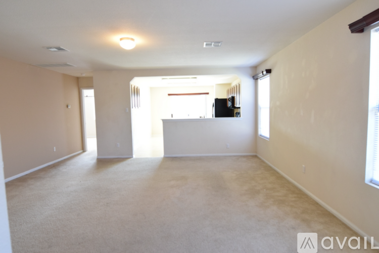 A spacious living room with a carpeted floor and a large window on the right side.