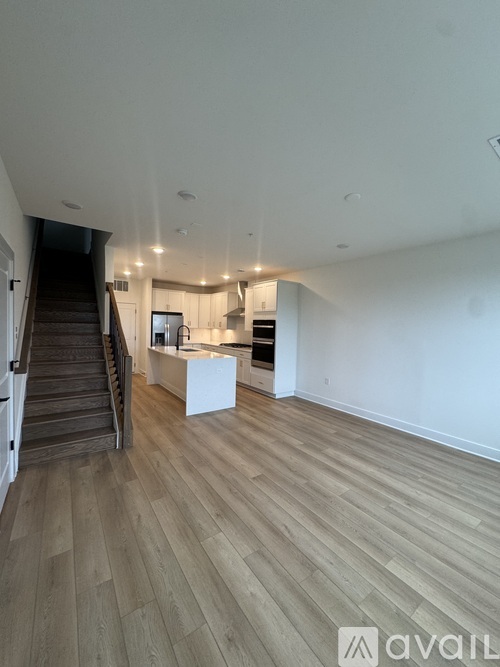 A spacious room with wooden flooring and a staircase leading to the upper level.