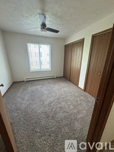 A room with a carpeted floor, a ceiling fan, and a window with blinds.