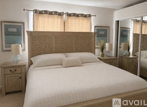 A bedroom with a large bed, a nightstand with a lamp, and a mirror.