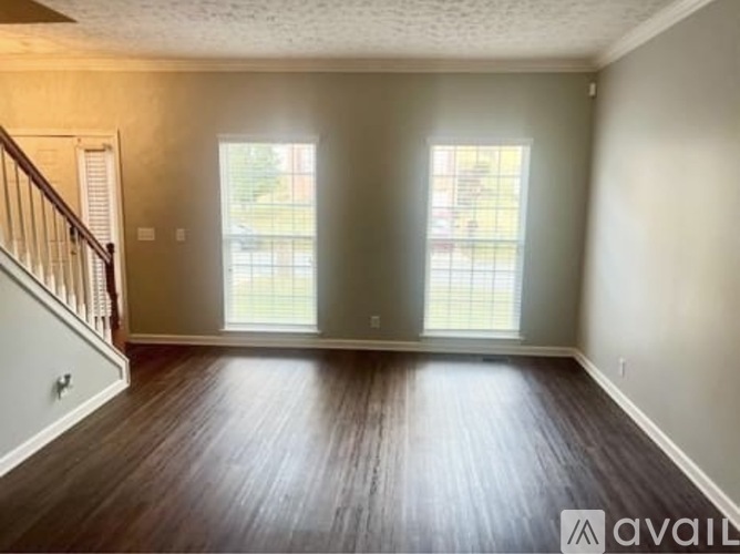A spacious room with wooden floors and two windows.