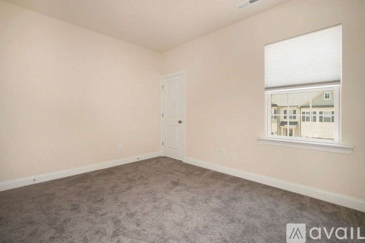 A room with a carpeted floor, a door, and a window showing a building outside.