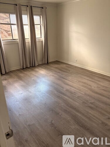 A room with wooden flooring and a window with curtains.