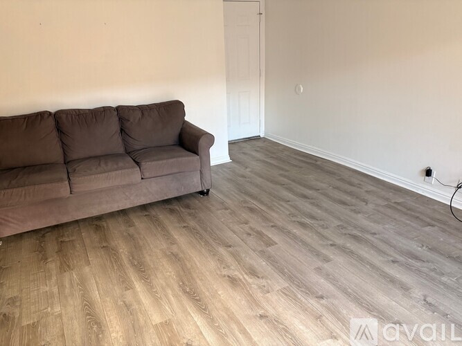A grey couch is placed in a room with wooden flooring and a white door.