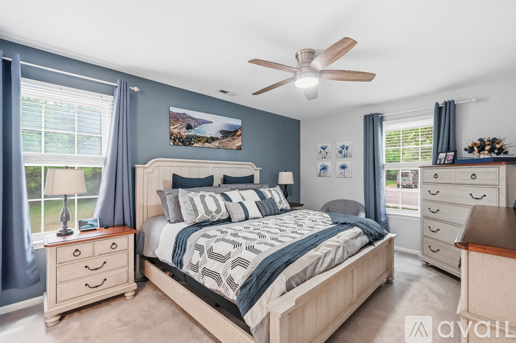 A bedroom with a large bed, a ceiling fan, and a painting on the wall.