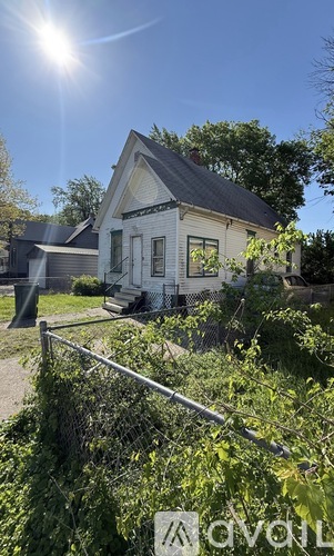 A house with a white facade and a grey roof is surrounded by greenery.