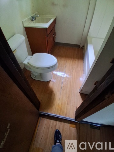 A white toilet sits in a small bathroom with wooden floors and a wooden cabinet.