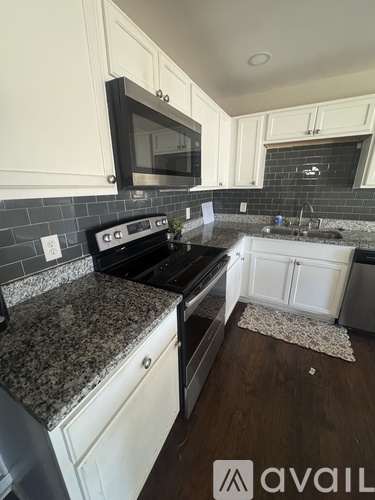 A kitchen with a black stove top oven and a black microwave above a granite counter.