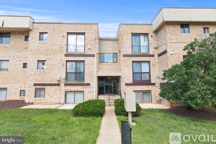 A multi-story apartment building with a grassy front yard and a walkway leading to the entrance.