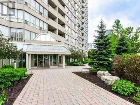 The image shows a building entrance with a walkway and some greenery.