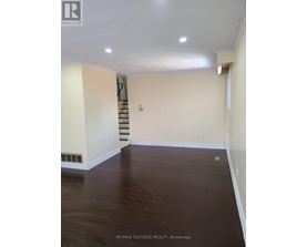 A room with a staircase in the background and a wooden floor.