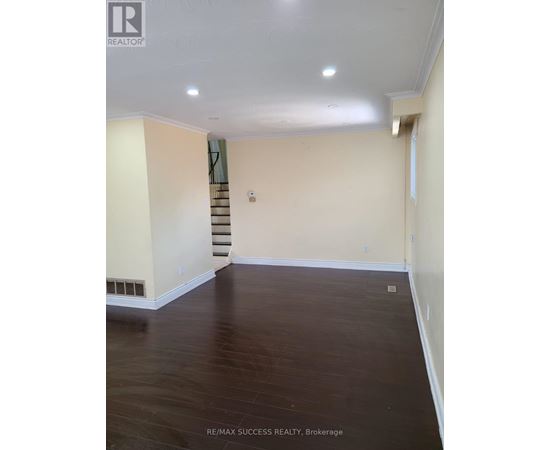 A room with a staircase in the background and a wooden floor.