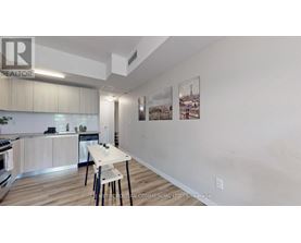 A kitchen with a dining table and chairs in the foreground and a wall with pictures hanging on it.