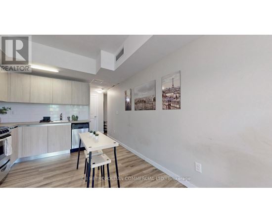 A kitchen with a dining table and chairs in the foreground and a wall with pictures hanging on it.