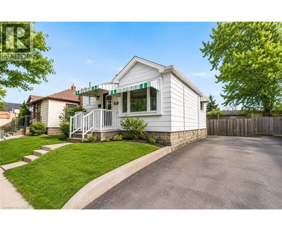 A white house with a green awning is surrounded by a wooden fence and a paved driveway.