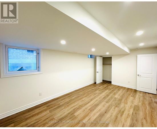 A room with wooden flooring and white walls, with a window showing a view of a building outside.