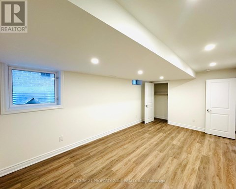 A room with wooden flooring and white walls, with a window showing a view of a building outside.