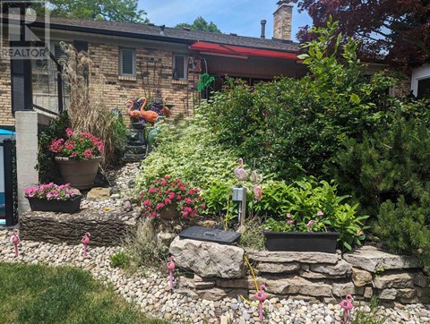 A garden with a stone wall and a house in the background.