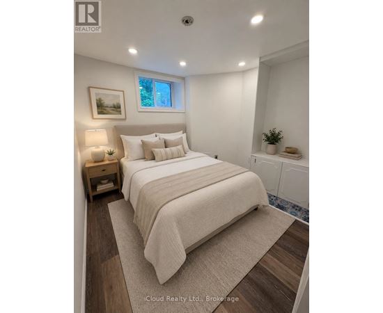 A bedroom with a large bed, a nightstand with a lamp, and a framed picture on the wall.