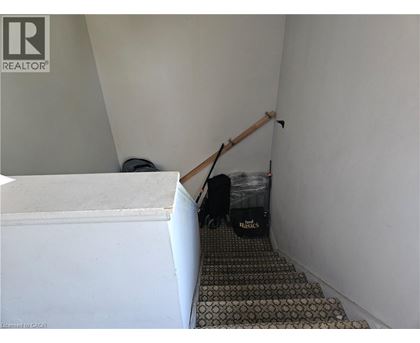 A room with a white wall and a trash can with a black bag of trash in it.