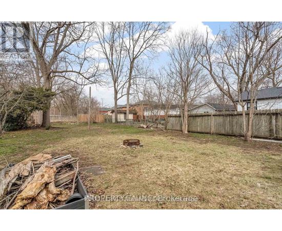 A backyard with a pile of wood in the foreground and a fence surrounding the yard.