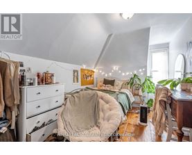 A bedroom with a bed covered in a blanket and a dresser with clothes hanging on it.