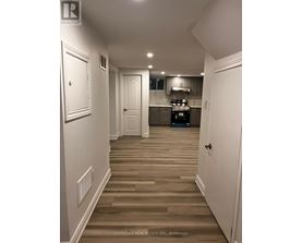 A hallway with white walls and wood flooring leads to a kitchen area.