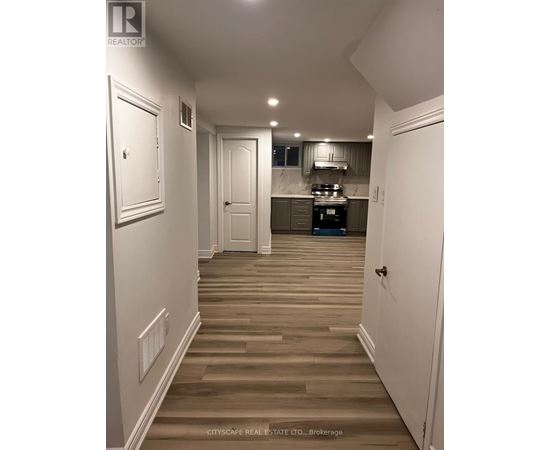 A hallway with white walls and wood flooring leads to a kitchen area.