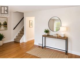 A room with a staircase, a table with a plant, and a round mirror on the wall.