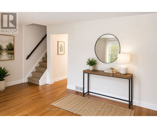 A room with a staircase, a table with a plant, and a round mirror on the wall.