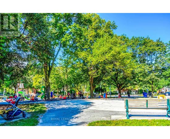 A park with a walking path, trees, and people.