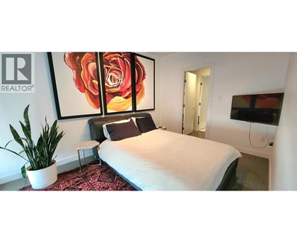 A bedroom with a large bed, a potted plant, and a painting of a rose.