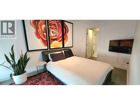 A bedroom with a large bed, a potted plant, and a painting of a rose.