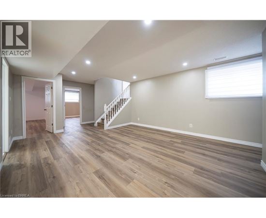 A spacious room with wooden flooring and a staircase.