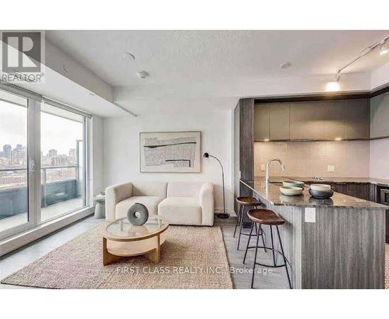 A modern living room with a large window and a kitchen area in the background.