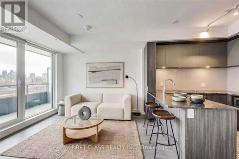 A modern living room with a large window and a kitchen area in the background.