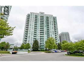 A tall building with many windows is surrounded by trees and a parking lot.